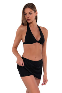 Side pose #1 of Daria wearing Sunsets Black Sporty Swim Skirt lifted up to show attached swim shorts with matching Faith Halter bikini top