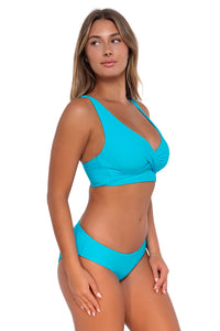 Side pose #1 of Taylor wearing Sunsets Blue Bliss Alana Reversible Hipster Bottom with matching Elsie Top underwire bikini