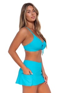 Side pose #1 of Taylor wearing Sunsets Blue Bliss Sporty Swim Skirt with hand in pocket and with matching Kauai Keyhole bikini top