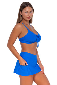 Side pose #1 of Taylor wearing Sunsets Electric Blue Sporty Swim Skirt with hand in pocket and with matching Kauai Keyhole bikini top