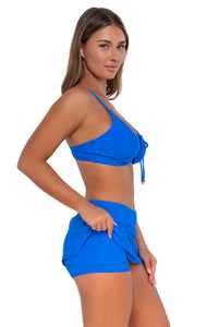 Side pose #1 of Taylor wearing Sunsets Electric Blue Sporty Swim Skirt lifted up to show attached swim shorts with matching Kauai Keyhole bikini top